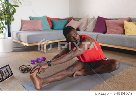 Happy african american man exercising, using tablet in living room 94984078