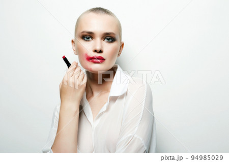 bald girl smearing red lipstick on her face. clown 94985029