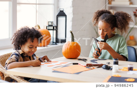 Happy ethnic children girl and boy making Halloween home decorations together 94986245
