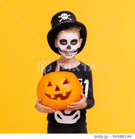 Happy cheerful boy in skeleton costume with pumpkin jack-o-lantern celebrates Halloween and laughs on yellow background 94986246