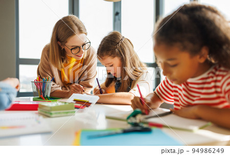 Teacher helping children with schoolwork at school Teacher helping children with schoolwork at school 94986249