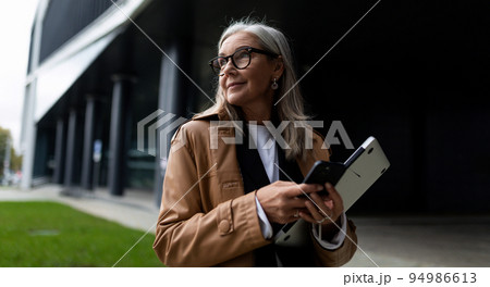 mature gray-haired businesswoman with a laptop in her hands on the background of the business center 94986613