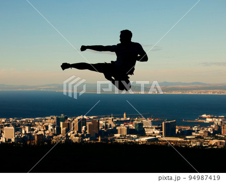 Silhouette of man doing karate with sky and city in the background. Outline of male athlete punching and kicking in the air in martial arts motion. Motivation, inspiration and urban warrior 94987419