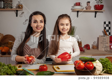Mother and her daughter are making a vegetable salad and having fun at the kitchen. 94989408