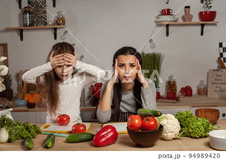 Mother and her daughter are making a vegetable salad and having fun at the kitchen. Mother and her daughter are making a vegetable salad and having fun at the kitchen. 94989420