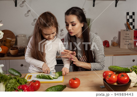 Mother and her daughter are making a vegetable salad and having fun at the kitchen. Mother and her daughter are making a vegetable salad and having fun at the kitchen. 94989443