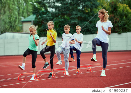 Female coach training athletes. Group of children running on treadmill at the stadium. Concept of sport, achievements, studying, goals, skills. Little boys and girls training outdoor. 94990287