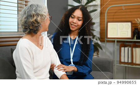 Elderly woman talking with caring young nurse, receiving home care physical and moral support. Home health care service concept Elderly woman talking with caring young nurse, receiving home care physical and moral support. Home health care service concept 94990655
