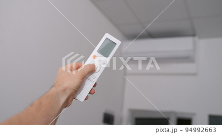 Hand with the remote control is directed to air conditioner Hand with the remote control is directed to air conditioner 94992663