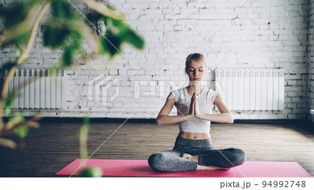 Attractive slim girl is practicing yoga in easy lotus pose on individual session in modern wellness center. Fexibility tranquility meditation concept. 94992748
