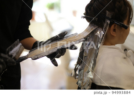 女性の髪のカラーリングをする男性美容師 94993884