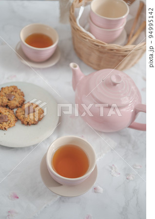 桜の花びらが散る中でティーカップに入った紅茶とクッキーでティータイム 94995142