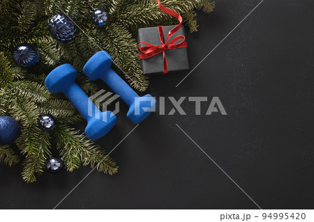 Christmas sport composition with blue sports dumbbells, gift, fir tree branches and Christmas gift 94995420