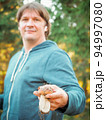 Satisfied young man holding a found porcini mushroom in his hands. The mushroom picker holds a cep mushroom. Man collect mushrooms in forest.  94997080