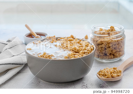 Dry breakfast cereals. Crunchy honey granola bowl and a glass of milk on a table. Healthy and fiber food. Dry breakfast cereals. Crunchy honey granola bowl and a glass of milk on a table. Healthy and fiber food. 94998720