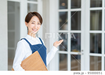 カフェの前でお客様を迎えるミドル女性 95000051