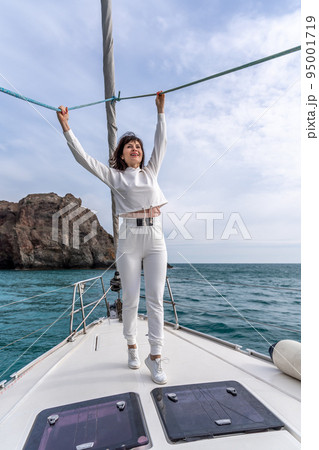 Woman standing on the nose of the yacht at a sunny summer day, breeze developing hair, beautiful sea on background 95001719