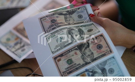 Counterfeiter cuts dollar bills with scissors closeup Counterfeiter cuts dollar bills with scissors closeup 95002859
