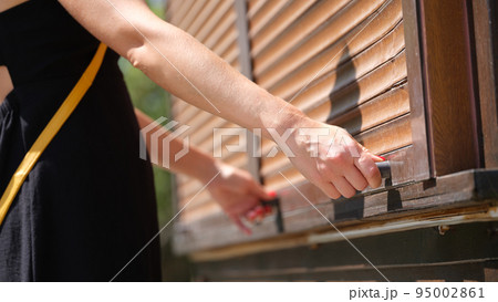 Female hands hold wooden latch handles open wooden blinds outdoors closeup 95002861