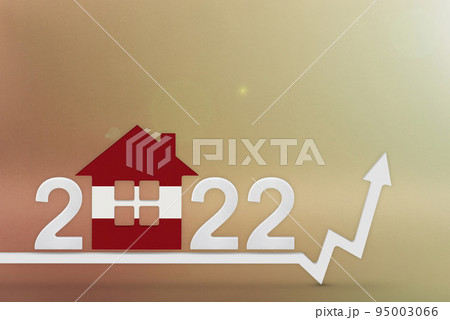 The cost of real estate in Latvia in 2022. Rising cost of construction, insurance, rent in Latvia. House model painted in flag colors, up arrow on yellow background 95003066
