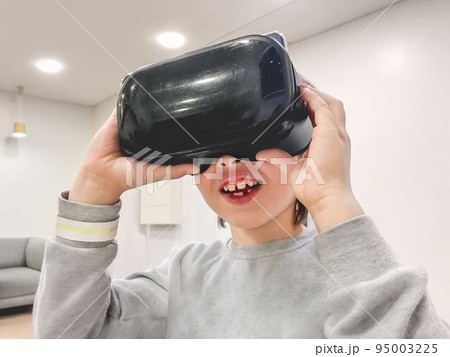 Smiling boy is watching something in VR-glasses. New technology for entertainment and developing skills. Device with usage of smartphone and application. 95003225