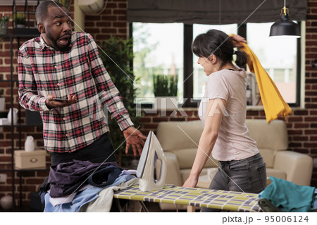 Woman fighting with husband at home, African American man trying to communicate with angry wife. Multiracial couple arguing about household chores, lack of help and collaboration. 95006124
