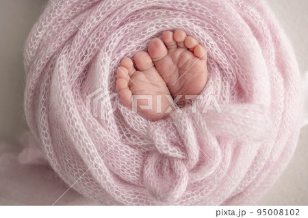 Knitted pink heart in the legs of a baby. Soft feet of a new born in a pink wool blanket. Close-up of toes, heels and feet of a newborn. Macro photography the tiny foot of a newborn baby.  Knitted pink heart in the legs of a baby. Soft feet of a new born in a pink wool blanket. Close-up of toes, heels and feet of a newborn. Macro photography the tiny foot of a newborn baby.  95008102