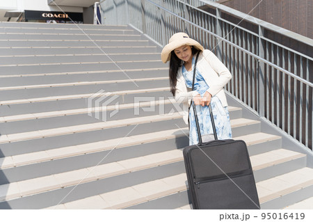 階段でスーツケースを引き上げる若い女性 95016419