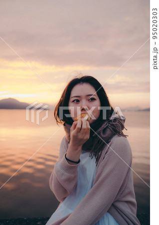 朝焼けが綺麗なパンを食べる女性の写真 95020303