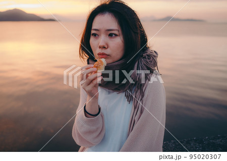 朝焼けが綺麗なパンを食べる女性の写真 95020307