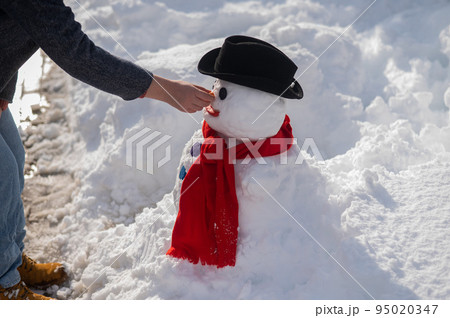 Caucasian woman sculpts a snowman from the snow. The carrot is the place of the nose. 95020347
