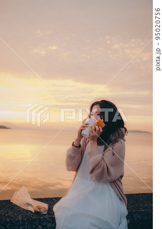 朝焼けが綺麗なパンを食べる女性の写真 95020756