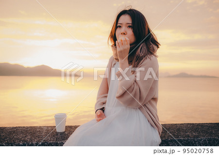 朝焼けが綺麗なパンを食べる女性の写真 95020758