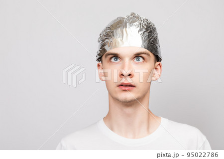 Paranoid young man wearing tin foil hat studio shot on gray background Paranoid young man wearing tin foil hat studio shot on gray background 95022786