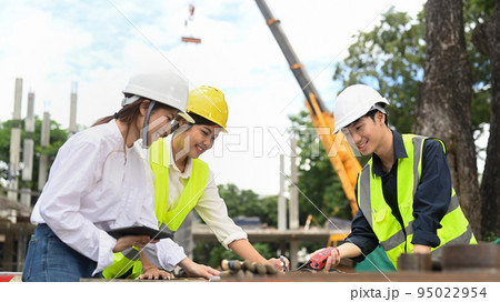 Engineer team discussing industrial building design project at construction site against mobile crane on background Engineer team discussing industrial building design project at construction site against mobile crane on background 95022954