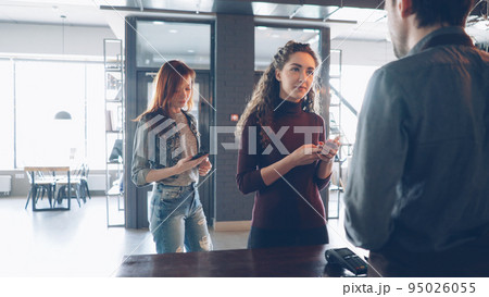 Busy work day at cozy coffeehouse with customers standing at counter buying coffee and friendly employees working and talking. 95026055