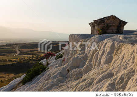 トルコ　ヒエラポリス・パムッカレの白い鍾乳石に咲いた花と石灰棚の上に建つ小屋 95026755