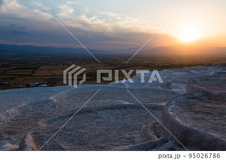トルコ　ヒエラポリス・パムッカレの石灰棚と夕焼けでオレンジに染まった空と石灰華段丘から見える風景 95026786