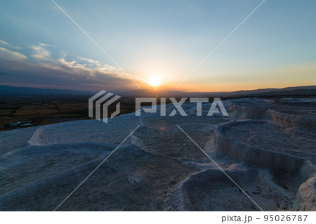 トルコ　ヒエラポリス・パムッカレの石灰棚と夕焼けでオレンジに染まった空と石灰華段丘から見える風景 95026787