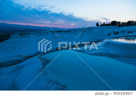 トルコ　夕暮れ時のヒエラポリス・パムッカレの石灰棚と青い水面 95026907