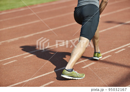 young asian man male athlete warming up stretching legs on track 95032167