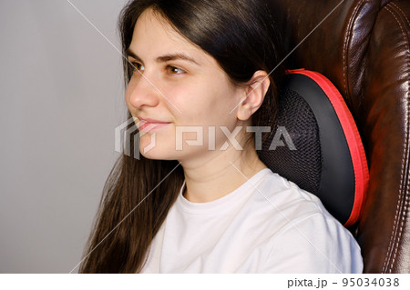 A woman sits in a chair with a massage pillow and does a neck massage. 95034038