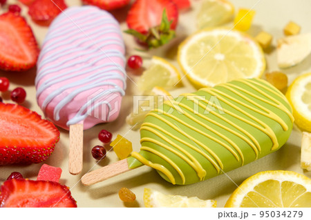 Two ice creams on a sticks - strawberry and lemon on a beige background. Summer fruit desserts. Two ice creams on a sticks - strawberry and lemon on a beige background. Summer fruit desserts. 95034279
