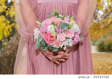 The bride in a pink dress holds a bouquet of pink and white roses in the autumn park close-up. 95034280