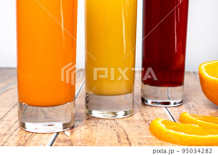 Three different fruit juices in glasses and fruits on a wooden background. Healthy nutrition for children and adults. Orange, cherry and tropical juice. 95034282