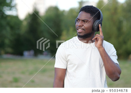 African American man listening to music walks in park 95034678
