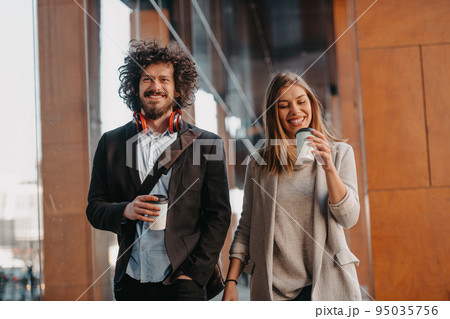 Business man and business woman talking and holding luggage traveling on a business trip, carrying fresh coffee in their hands.Business concept Business man and business woman talking and holding luggage traveling on a business trip, carrying fresh coffee in their hands.Business concept 95035756
