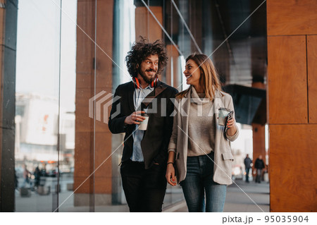 Business man and business woman talking and holding luggage traveling on a business trip, carrying fresh coffee in their hands.Business concept Business man and business woman talking and holding luggage traveling on a business trip, carrying fresh coffee in their hands.Business concept 95035904