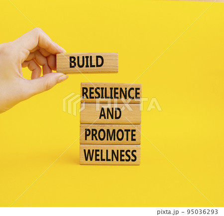 Resilience and Wellness symbol. Wooden blocks with words Build Resilience and Promote Wellness. Businessman hand. Beautiful yellow background. Build Resilience and Promote Wellness. Copy space 95036293