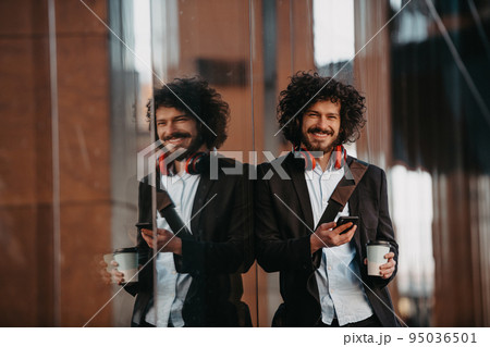 Trendy businessman with leather briefcase in financial district using smartphone while listening audio songs headphones drinking coffee 95036501